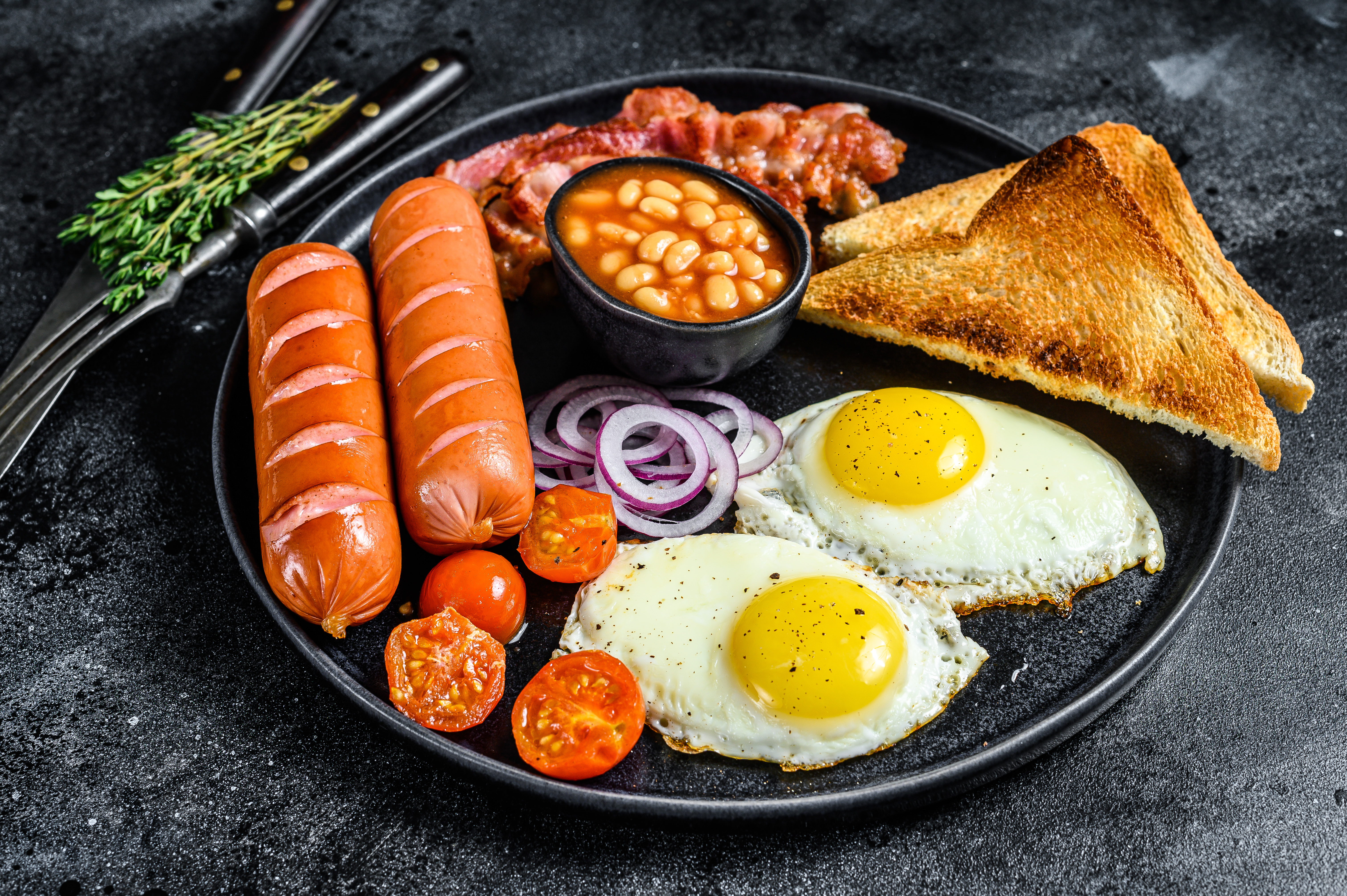 English breakfast with fried eggs, sausages, bacon, beans and toasts in a plate.